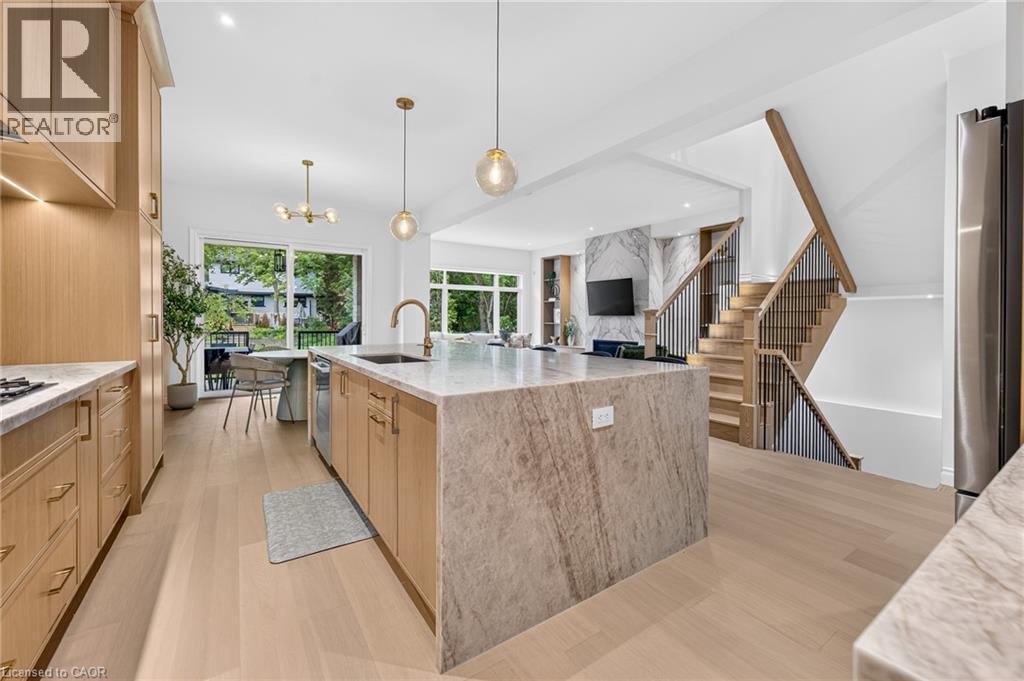 Hardwood flooring throughout, kitchen island with stone countertop, wood cabinetry with gold-tone hardware, built-in stainless steel appliances, and a staircase with wood and metal railings - 67 Cielo Court, Hamilton, ON