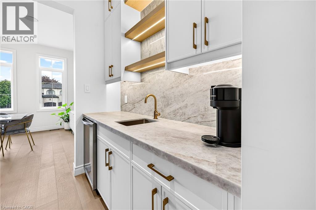 Built-in beverage station featuring a sink with a gold-finish faucet, undercabinet lighting, and stone backsplash - 67 Cielo Court, Hamilton, ON
