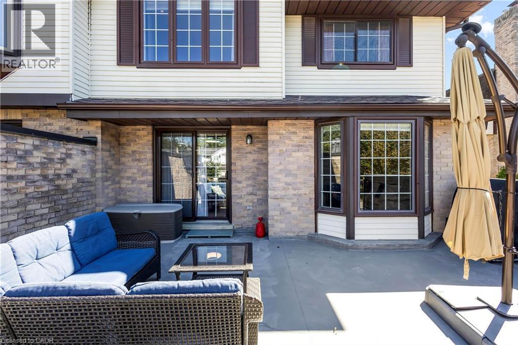 Expansive patio with brick and siding exterior, featuring a hot tub, sliding glass door access, and a bay window - 475 Beechwood Drive Unit# 4, Waterloo, ON