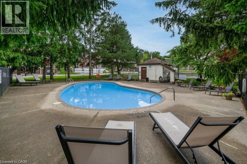 Outdoor swimming pool with concrete surround, bordered by mature trees and a privacy fence - 475 Beechwood Drive Unit# 4, Waterloo, ON
