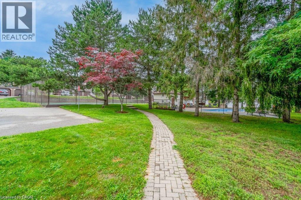 Expansive green lawn with a paver pathway, mature trees, and a tennis court - 475 Beechwood Drive Unit# 4, Waterloo, ON