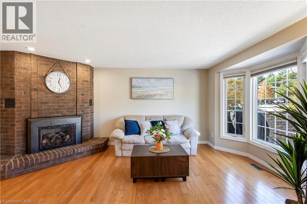 Angled brick fireplace with a black metal insert, natural wood flooring, and a multi-pane bay window - 475 Beechwood Drive Unit# 4, Waterloo, ON