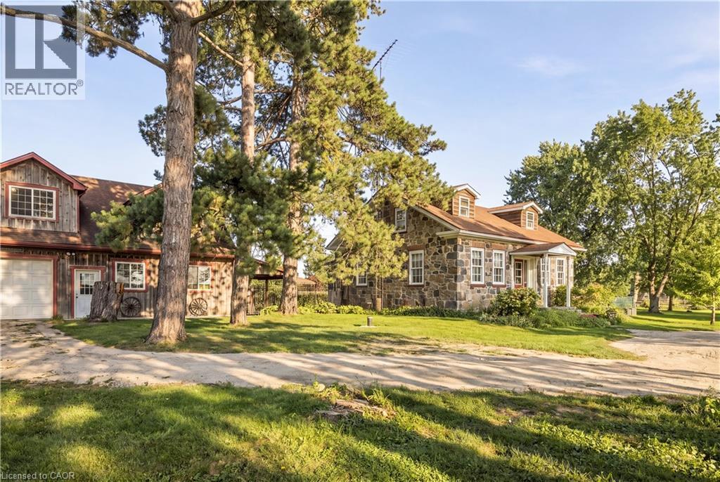 Stone exterior residence with a covered front porch, dormer windows, and a detached two-story structure featuring a garage door and siding - 2744 Bleams Road, New Hamburg, ON
