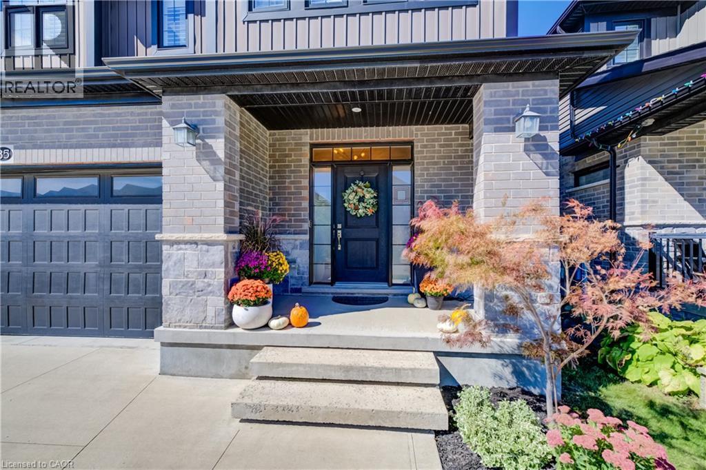Brick and vertical siding exterior with a covered entry, concrete steps, and a dark paneled garage door - 35 Greyhawk Street, Kitchener, ON