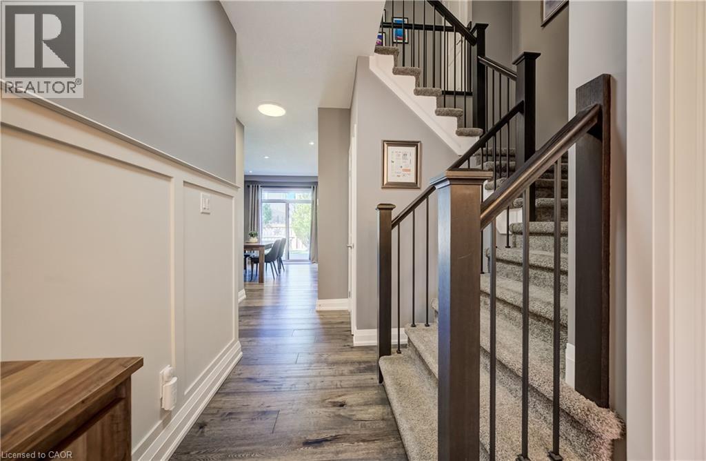 Wood-finish flooring throughout the hallway, wainscoting detail on the wall, and a staircase with metal balusters and carpeted treads - 35 Greyhawk Street, Kitchener, ON