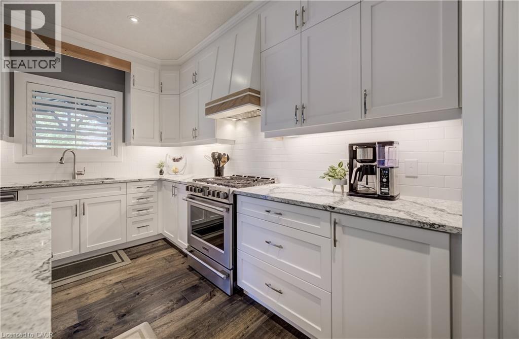 White shaker-style cabinetry with ample storage, polished granite countertops, white subway tile backsplash, stainless steel range, and wood-finish flooring - 35 Greyhawk Street, Kitchener, ON