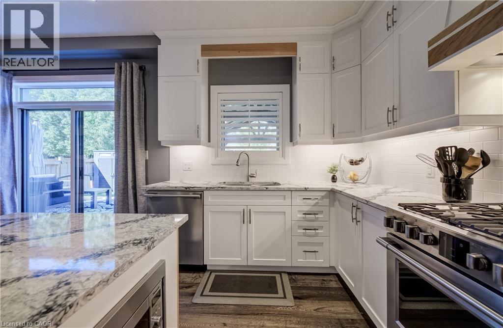 White cabinetry with contrasting hardware, light-toned countertops, subway tile backsplash, stainless steel appliances, and wood-finish flooring - 35 Greyhawk Street, Kitchener, ON