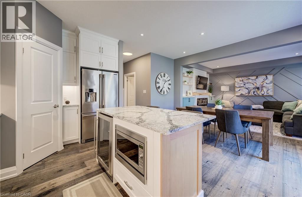 Open-concept living area with wood-finish flooring, a kitchen island featuring a light-toned countertop, and stainless steel appliances - 35 Greyhawk Street, Kitchener, ON