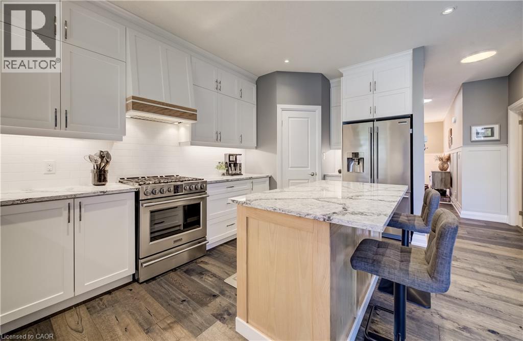 White shaker cabinetry, light-toned wood-finish flooring, stainless steel range, stainless steel refrigerator, and light-toned countertop - 35 Greyhawk Street, Kitchener, ON