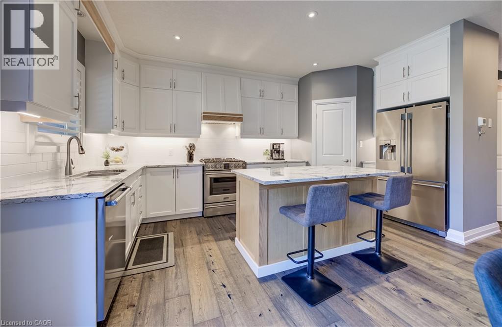 Kitchen featuring white cabinetry, stainless steel appliances, wood-finish flooring, a central island with a stone countertop, and recessed lighting - 35 Greyhawk Street, Kitchener, ON