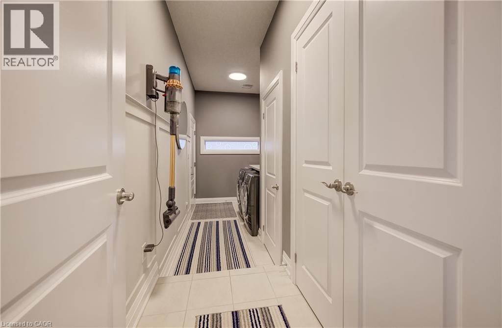Laundry area featuring light tile flooring, a horizontal window, and panel doors with satin nickel hardware - 35 Greyhawk Street, Kitchener, ON