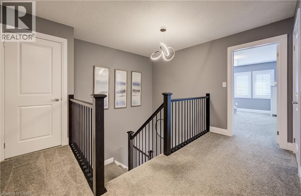Upper-level landing featuring textured carpeting, neutral wall colors, contemporary ceiling fixture, and dark wood newel posts with iron balusters - 35 Greyhawk Street, Kitchener, ON