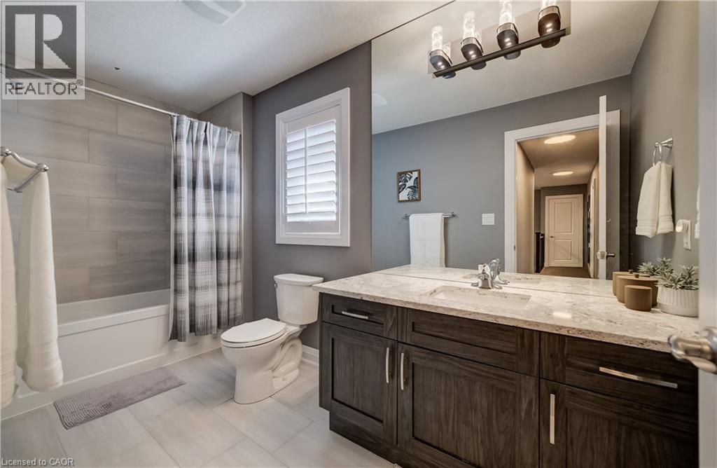 Bathtub and shower combination with full tile surround, wood-finish vanity with countertop, large wall-mounted mirror, and tile flooring - 35 Greyhawk Street, Kitchener, ON