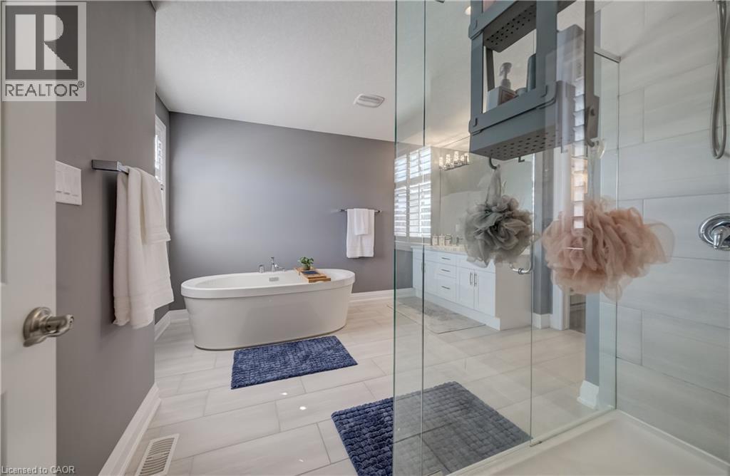 Freestanding soaking tub, glass-enclosed shower, dual vanity with shaker-style cabinetry, tiled flooring, and window with plantation shutters - 35 Greyhawk Street, Kitchener, ON