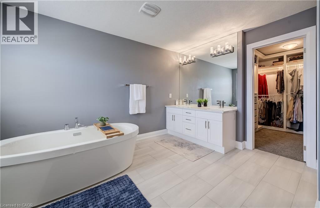 Freestanding soaking tub, double vanity with white cabinetry, light gray tile flooring, and integrated walk-in closet with built-in shelving - 35 Greyhawk Street, Kitchener, ON