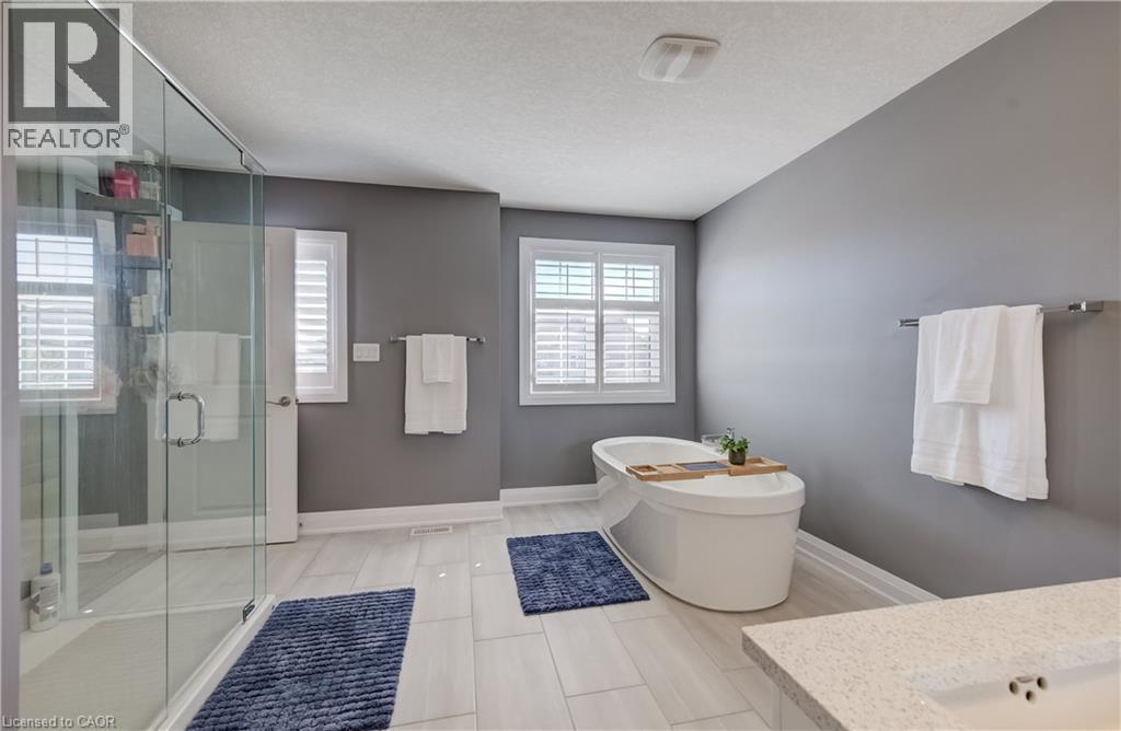 Freestanding soaking tub, glass-enclosed shower, dual windows with plantation shutters, light gray wall finish, and stone-finish countertop with integrated sink - 35 Greyhawk Street, Kitchener, ON