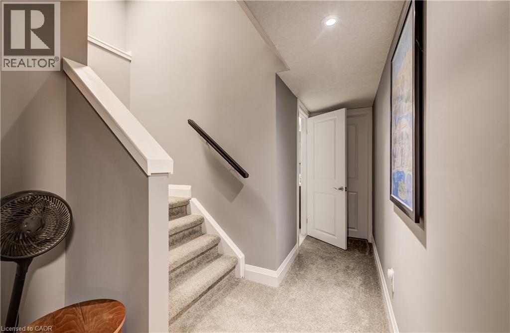 Staircase with carpeted treads, white newel post, and black wall-mounted handrail - 35 Greyhawk Street, Kitchener, ON