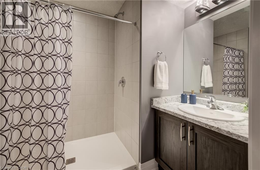 Walk-in shower with tiled walls and a white base, complemented by a vanity featuring a granite-look countertop and an integrated sink - 35 Greyhawk Street, Kitchener, ON