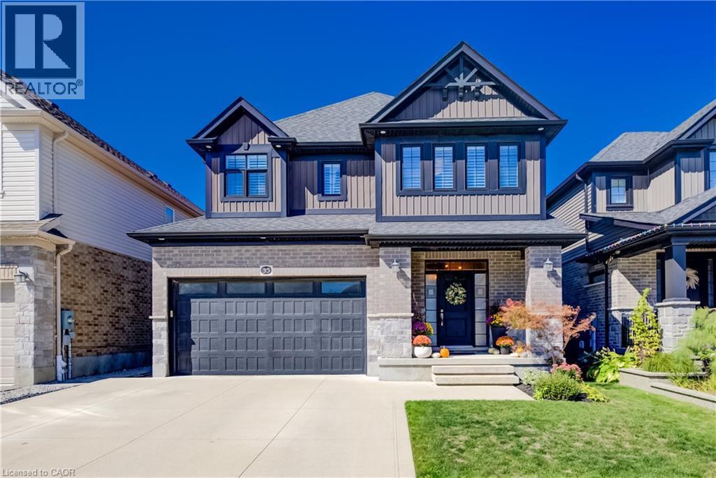 Two-story residence featuring a dark paneled garage door, a covered front entry, light brick and dark siding exterior, and a paved driveway - 35 Greyhawk Street, Kitchener, ON