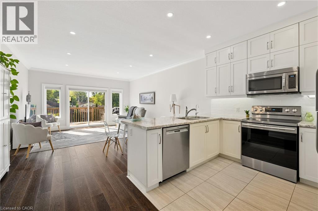 Open-concept living area with dark wood-finish flooring, white shaker cabinetry, stainless steel appliances, and a sliding glass door to an outdoor deck - 192 Brewery Street Unit# 18, Baden, ON