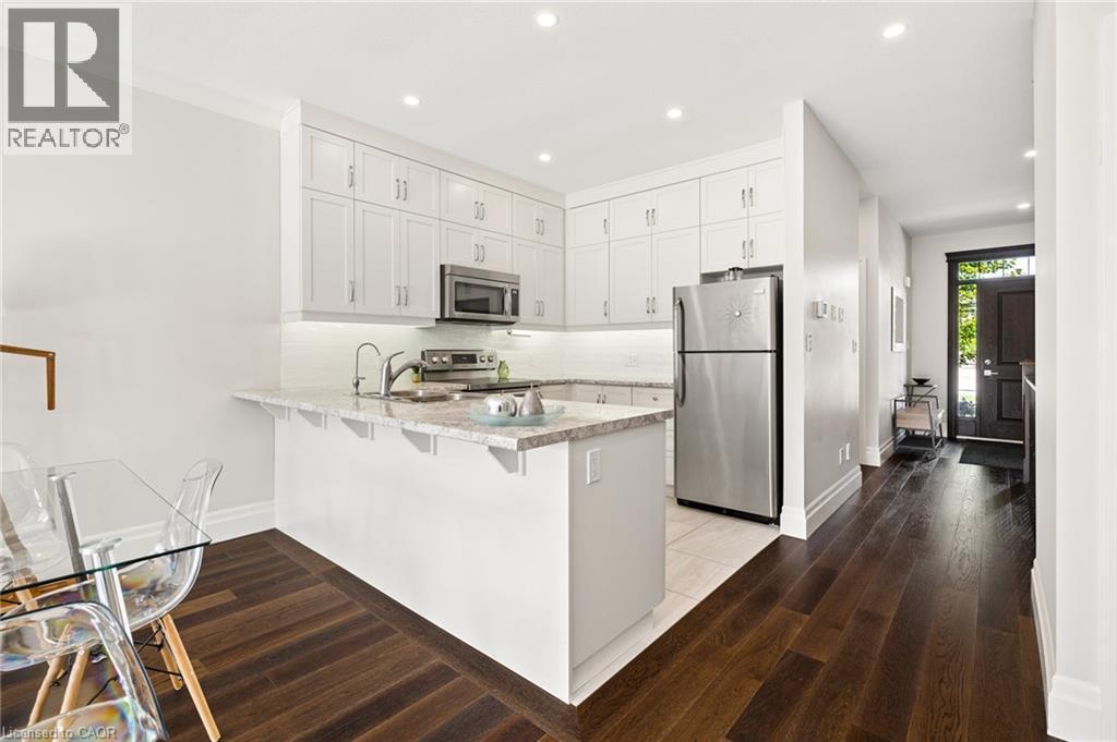 Kitchen featuring white cabinetry, stainless steel appliances, light-toned countertops, a breakfast bar, and dark wood-finish flooring - 192 Brewery Street Unit# 18, Baden, ON