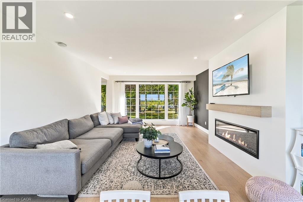 Recessed lighting illuminating the room, wood-finish flooring, large multi-pane windows, built-in linear fireplace with a wood mantle, and a contrasting accent wall - 5367 2 Side Road, Milton, ON