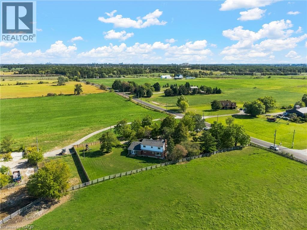 Expansive property featuring a two-story residence with a red brick facade, surrounded by a large green lawn and mature trees - 5367 2 Side Road, Milton, ON