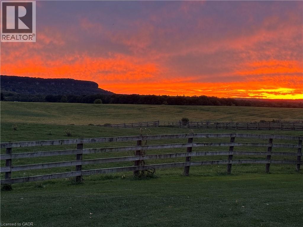 Expansive green fields with natural wood fencing, framed by distant hills and a vibrant sunset sky - 5367 2 Side Road, Milton, ON