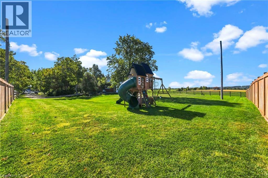 Expansive yard featuring a vibrant green lawn, wood privacy fencing, and a playset with a slide - 5367 2 Side Road, Milton, ON