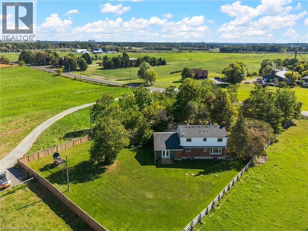 Expansive green landscape with a two-story residence featuring a white and brick exterior, a dark shingled roof, and multiple windows - 5367 2 Side Road, Milton, ON