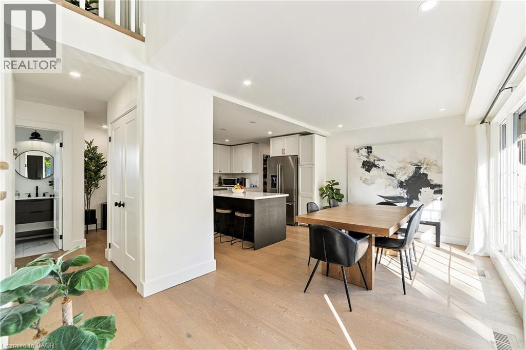 Open-concept main level featuring wood-finish flooring, a modern kitchen island with seating, recessed lighting, and a powder room with a vanity and round mirror - 5367 2 Side Road, Milton, ON