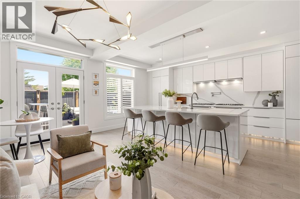 Modern kitchen featuring an island with seating, white flat-panel cabinetry, integrated appliances, and a linear pendant light - 5056 New Street Unit# 4, Burlington, ON