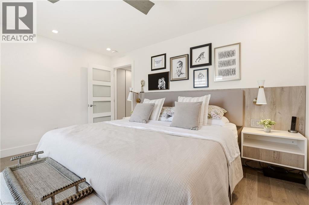 Recessed lighting, wood-finish flooring, accent wall with paneling, built-in wall sconces, and a modern four-panel door - 5056 New Street Unit# 4, Burlington, ON