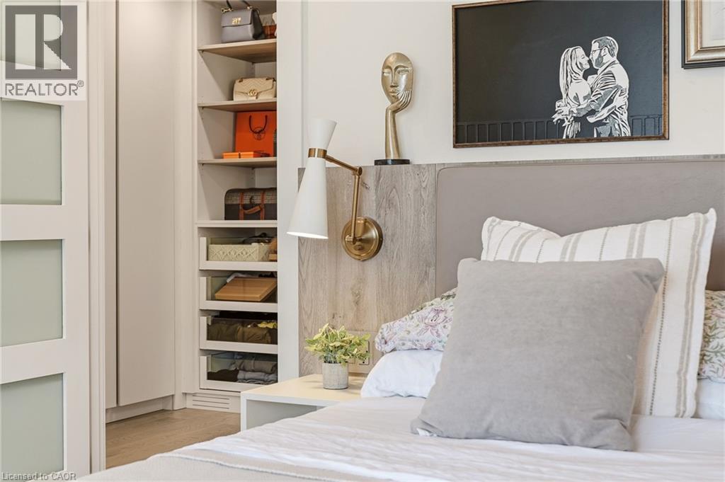 Custom built-in closet with integrated shelving, wood-finish flooring, wall-mounted sconce, and upholstered headboard - 5056 New Street Unit# 4, Burlington, ON