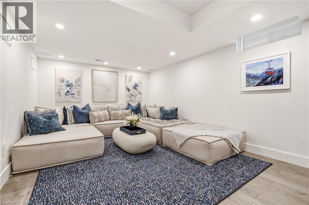 Sophisticated recreation room showcasing a sectional seating arrangement with coordinating throw pillows, recessed ceiling lighting, wood-finish flooring, a geometric patterned area rug, and framed ar - 5056 New Street Unit# 4, Burlington, ON