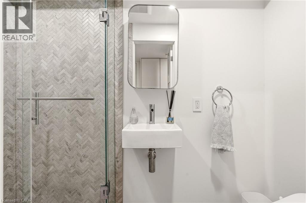 Glass-enclosed shower with herringbone tile, wall-mounted sink, and modern mirror - 5056 New Street Unit# 4, Burlington, ON