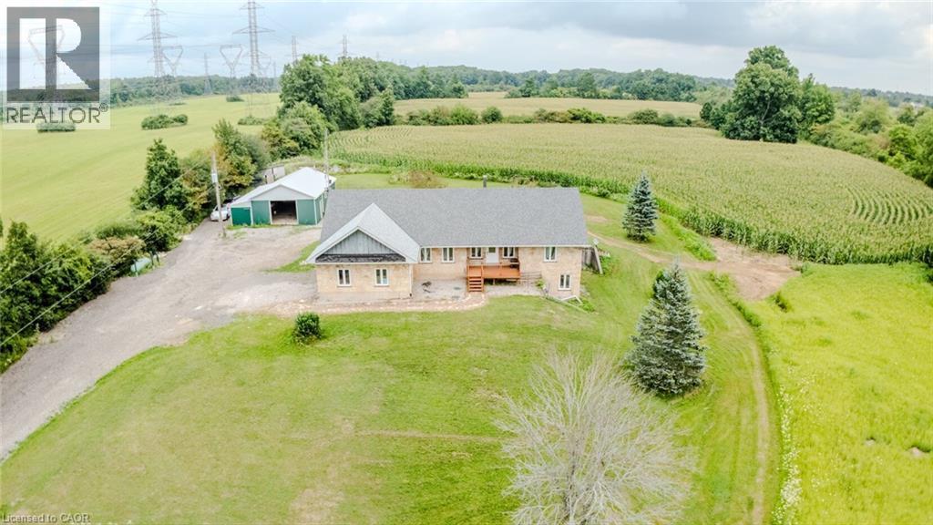 Stone exterior property with a shingled roof, featuring a wooden deck, mature evergreen trees, and an expansive lawn - 107 6Th Line Line, Haldimand, ON - Outdoor With View