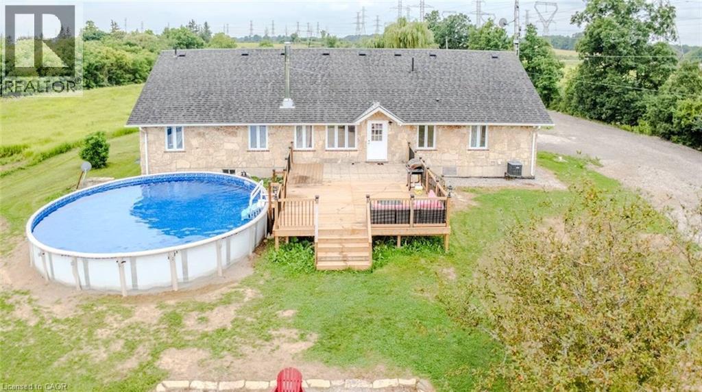 Stone exterior with a dark shingle roof, accompanied by a wooden deck and an oval above-ground pool - 107 6Th Line Line, Haldimand, ON - Outdoor With Above Ground Pool
