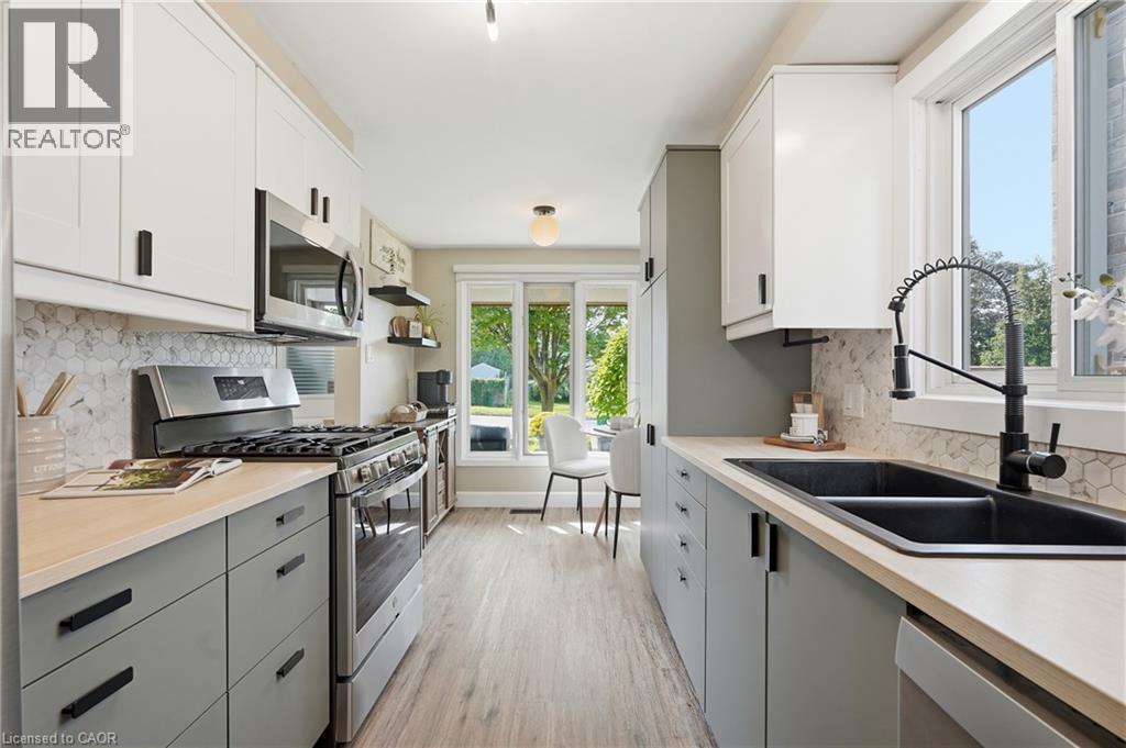 Contemporary kitchen featuring dual-tone cabinetry, stainless steel appliances, a double basin sink, and wood-finish flooring - 563 Westvale Drive, Waterloo, ON - Indoor Photo Showing Kitchen With Double Sink With Upgraded Kitchen