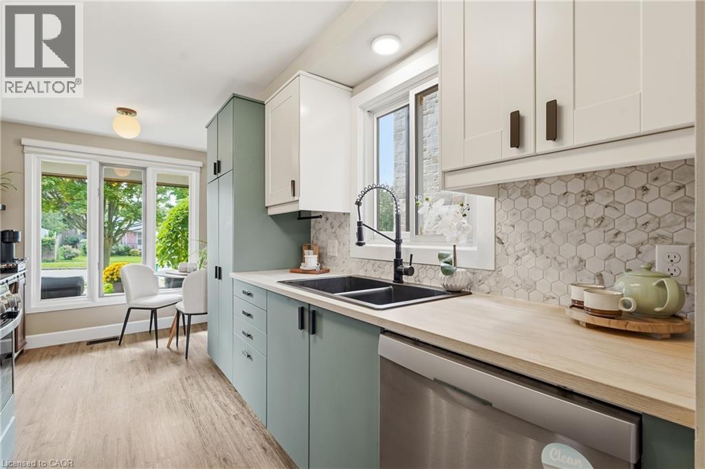 Kitchen featuring two-tone cabinetry, wood-finish flooring, a double basin sink with a gooseneck faucet, hexagon tile backsplash, and a built-in dishwasher - 563 Westvale Drive, Waterloo, ON - Indoor Photo Showing Kitchen With Double Sink With Upgraded Kitchen