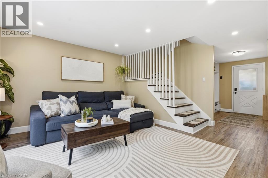 Recessed ceiling lighting, wood-finish flooring, white staircase with dark treads, white spindle railing, and a white paneled entry door with frosted glass - 563 Westvale Drive, Waterloo, ON - Indoor Photo Showing Living Room