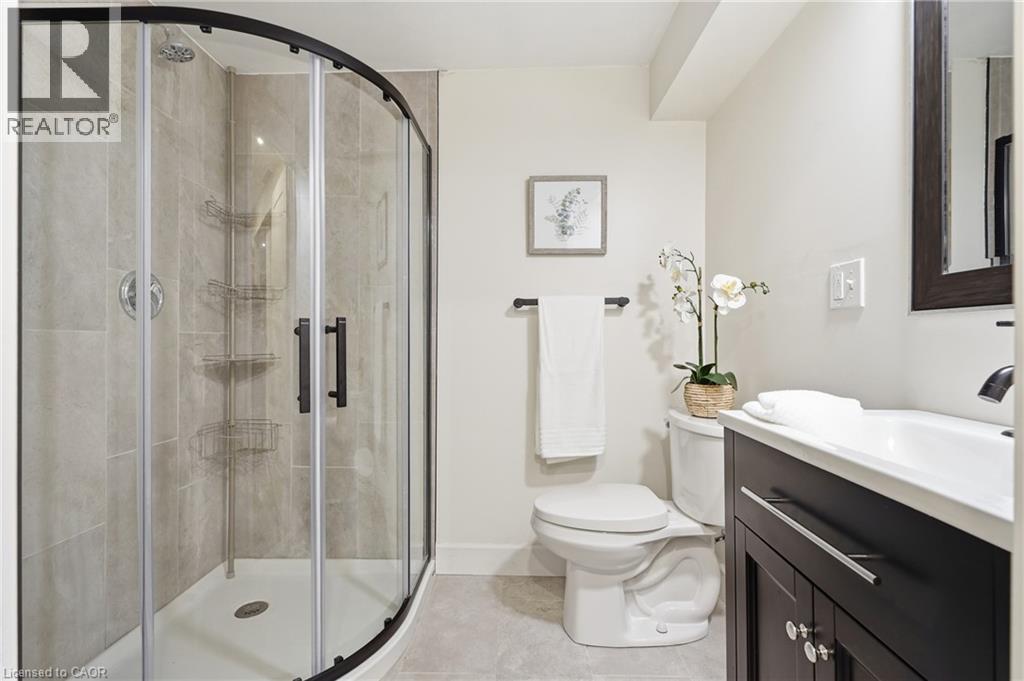 Curved glass shower enclosure with matte black trim, tiled shower surround, dark wood-finish vanity with an integrated basin sink, and a wall-mounted mirror - 563 Westvale Drive, Waterloo, ON - Indoor Photo Showing Bathroom