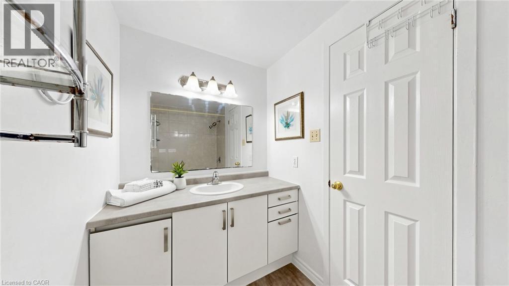 White paneled cabinetry with modern hardware, a countertop with an integrated sink, a rectangular mirror, and a four-light vanity fixture - 304 Bluevale Street N, Waterloo, ON - Indoor Photo Showing Bathroom