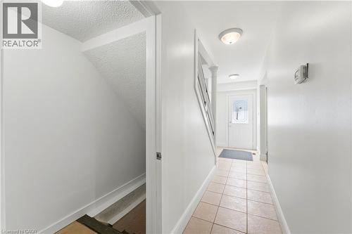 Hallway with neutral tone tile flooring, a staircase with a white railing, and a white front entry door with decorative glass - 23 Heatherdale Place, Hamilton, ON - Indoor Photo Showing Other Room