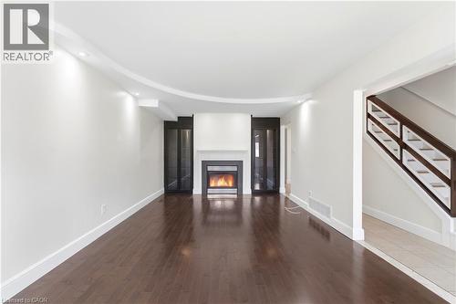Spacious room featuring wood-finish flooring, a built-in fireplace with a white mantel, recessed lighting, and built-in glass-front cabinetry - 23 Heatherdale Place, Hamilton, ON - Indoor With Fireplace
