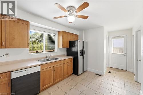 Kitchen featuring wood cabinetry, a double basin sink, a ceiling fan with light, tiled flooring, and a rear exterior door - 23 Heatherdale Place, Hamilton, ON - Indoor Photo Showing Kitchen With Double Sink