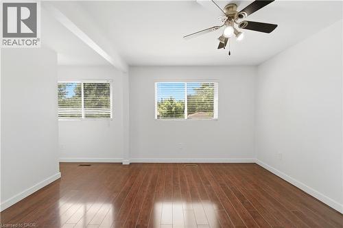 Wood-finish flooring, white walls, two windows with horizontal blinds, and a ceiling fan with integrated lighting - 23 Heatherdale Place, Hamilton, ON - Indoor Photo Showing Other Room