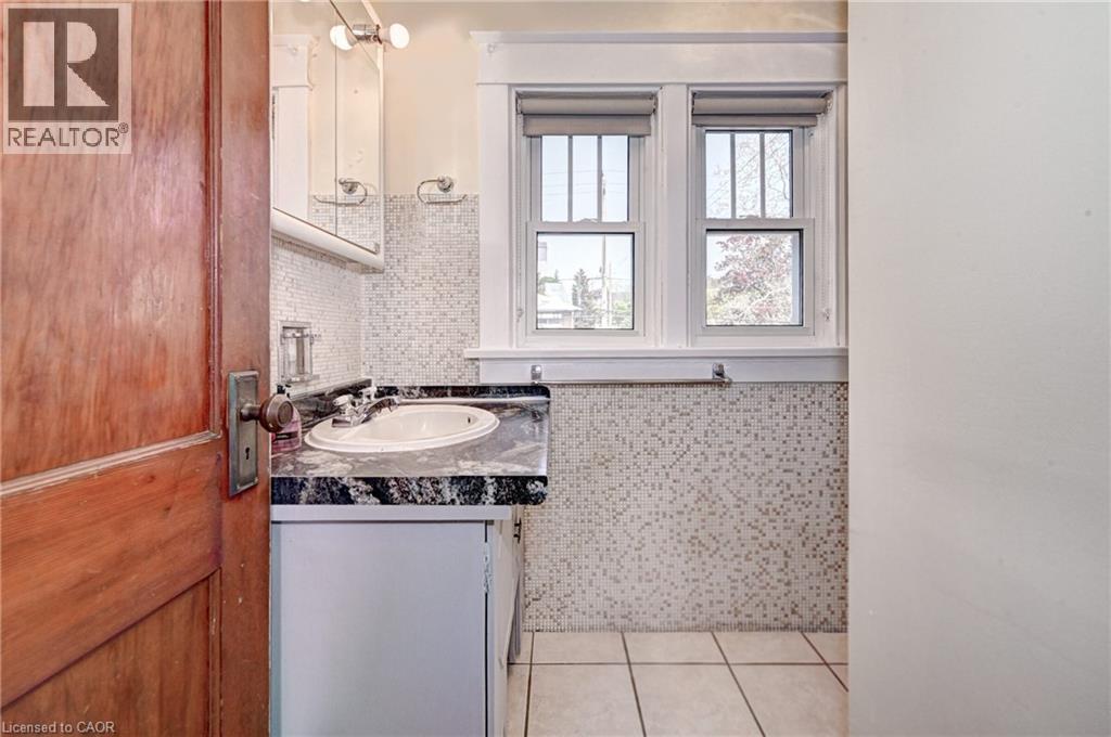 Compact bathroom featuring an integrated sink with a dark stone countertop, white vanity cabinetry, mosaic tile wainscoting, and a white tile floor - 147 Courtland Avenue E, Kitchener, ON - Indoor Photo Showing Bathroom