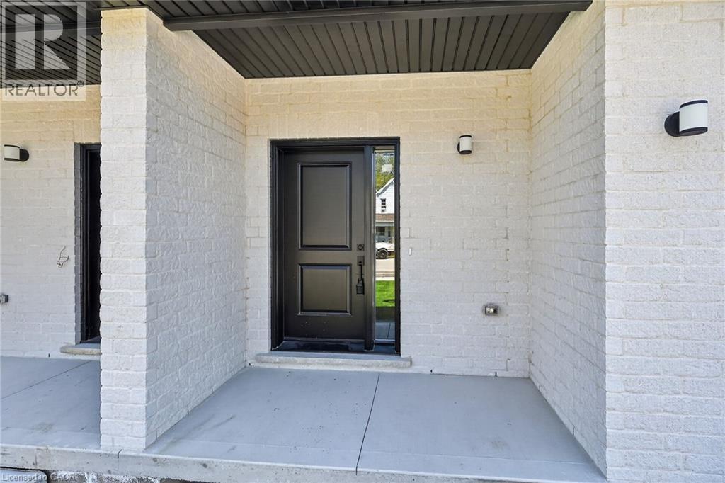 Contemporary entry featuring a black paneled door with sidelight, white painted brick facade, concrete porch, and black outdoor sconces - 45B Howard Street, Hagersville, ON