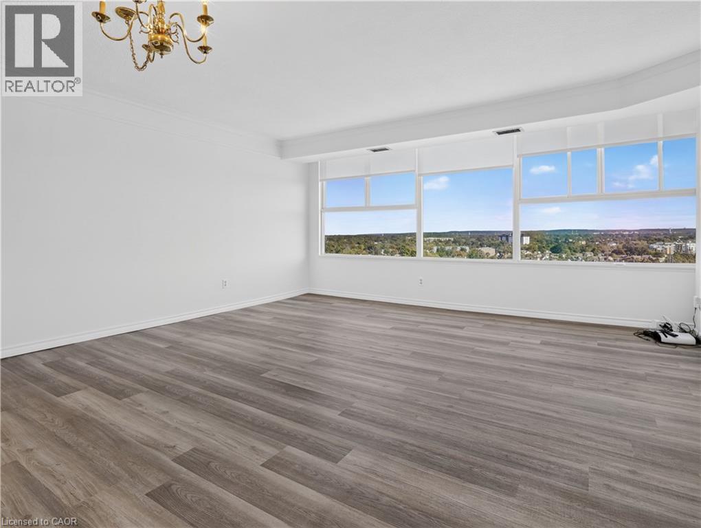 Spacious room featuring wood-finish flooring, extensive window line, and a decorative chandelier - 7 Gale Crescent Unit# 1107, St. Catharines, ON